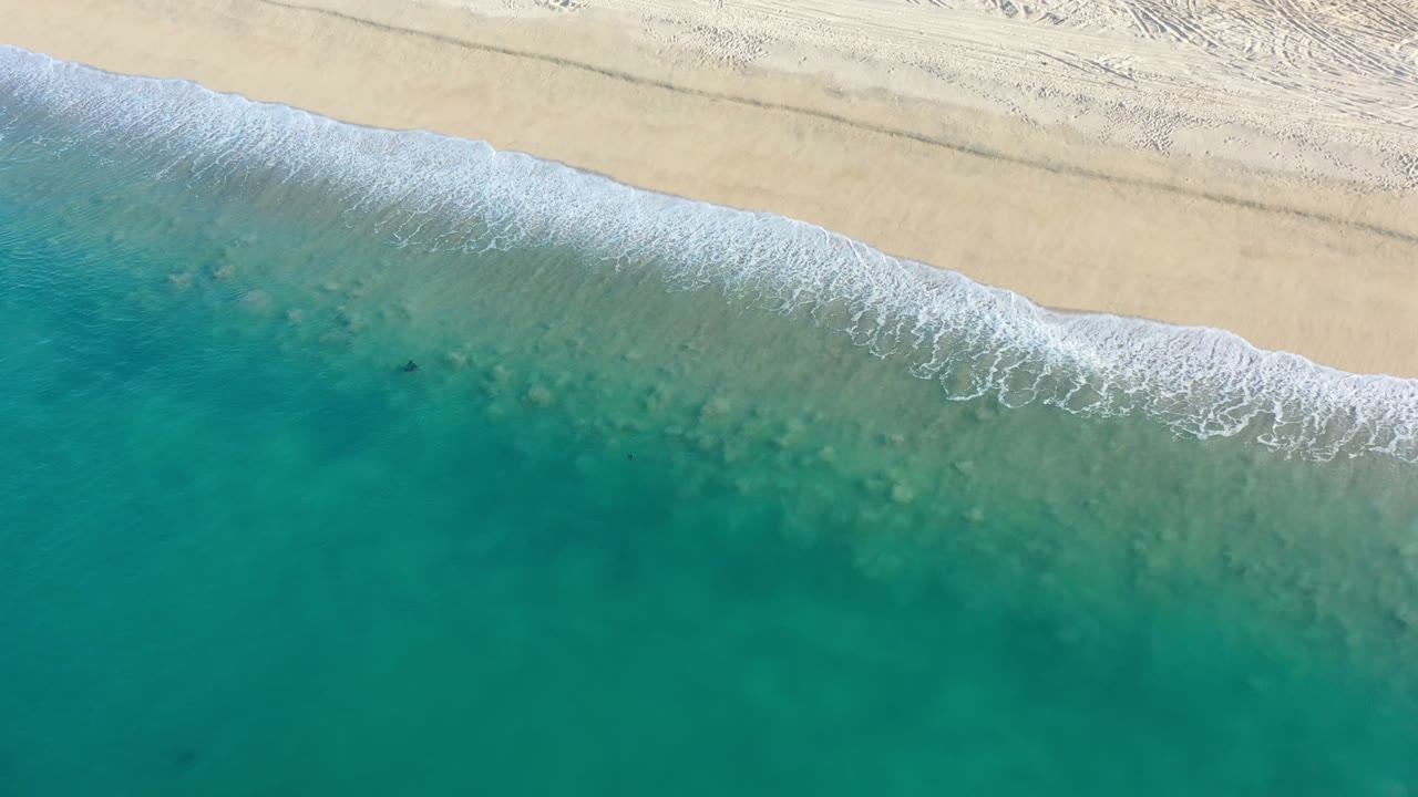 Overhead view of emerald water meeting pale sand