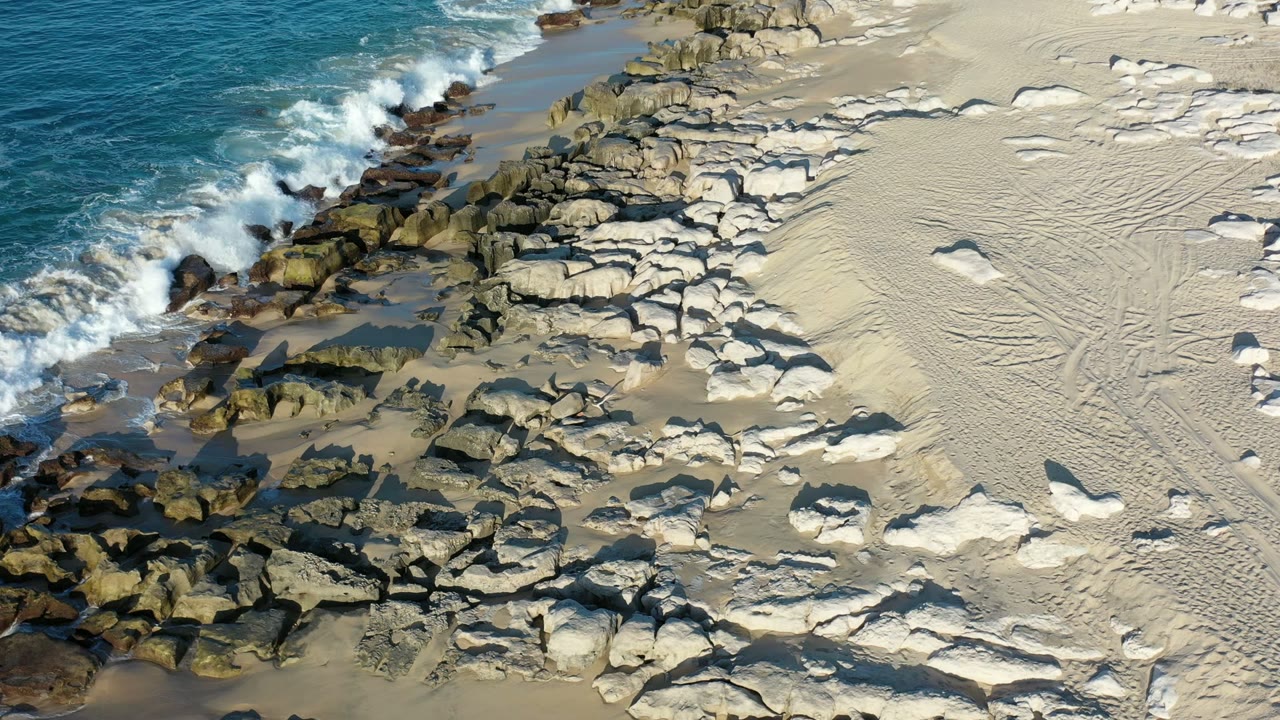 Surf breaking beside rocks and pale sand