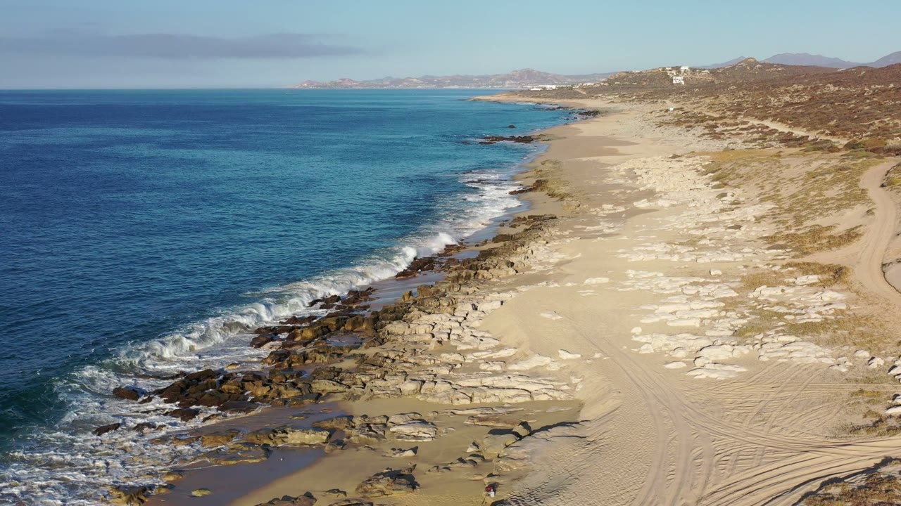 Elevated view of blue ocean meeting a sandy rocky beach.