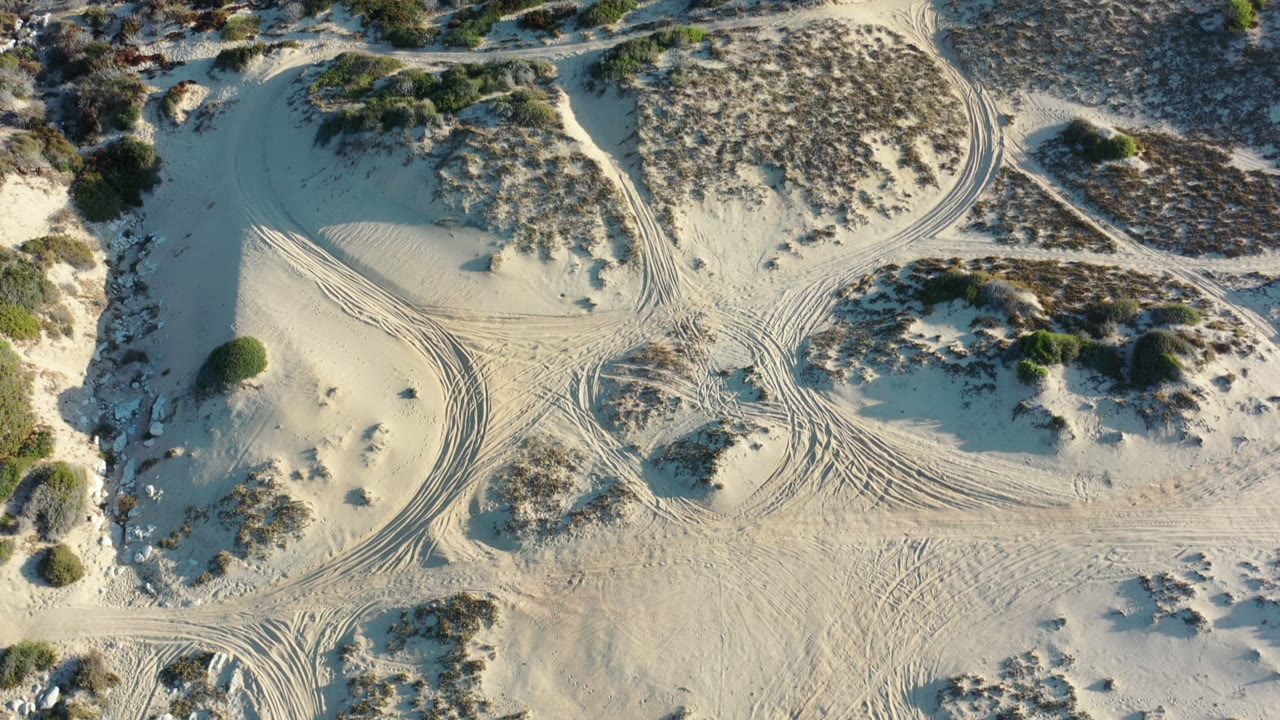Overhead sandy dunes with scrub bushes and tire tracks.