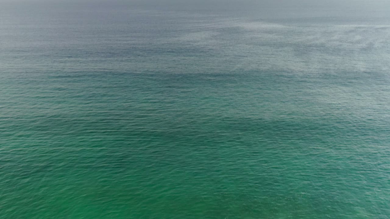Turquoise-green water fills the Los Cabos frame, with a faint horizontal break near the top and no visible people or vessels.