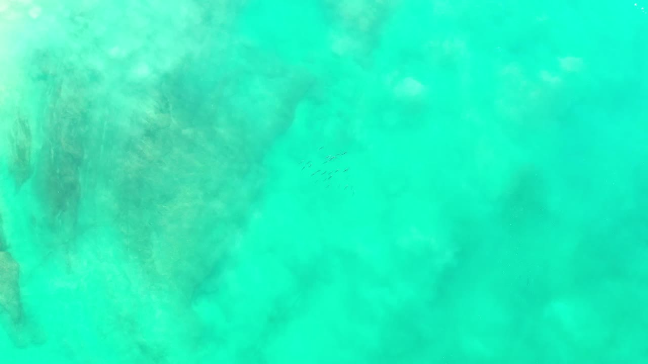 Overhead Los Cabos sea view with cloudy pale water texture, darker green areas below the surface, and no visible people.