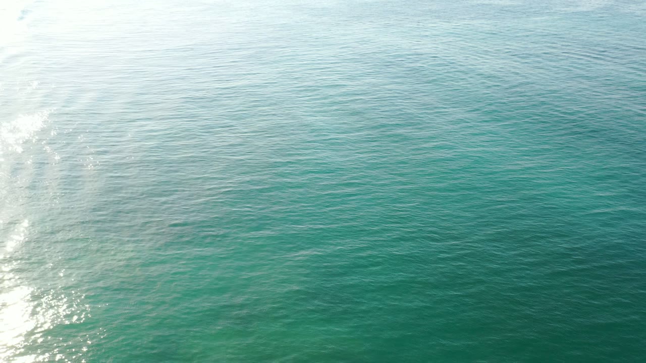 Aerial view of blue-green ocean water with sun glare and small waves.