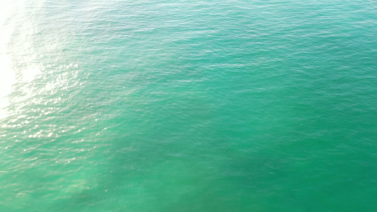 Turquoise ocean surface in Los Cabos, Mexico, with a bright band of reflected sunlight crossing the left side and no visible people.