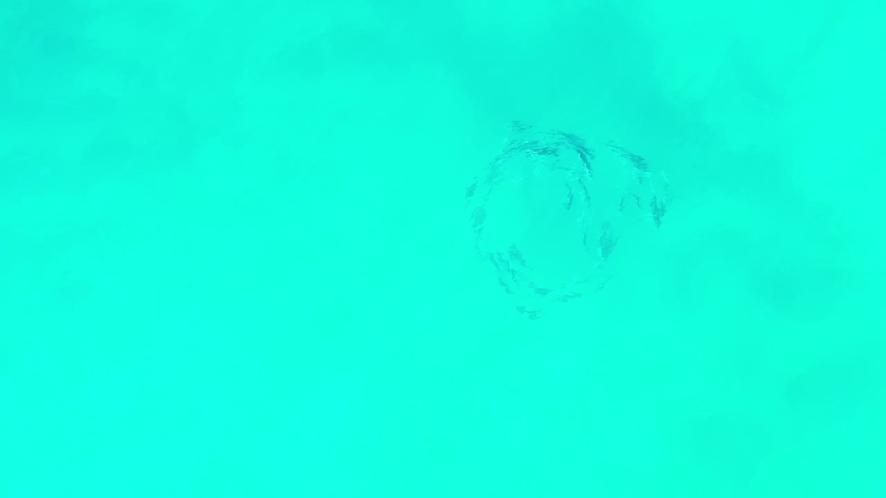Turquoise ocean water in Los Cabos, Mexico, with a small faint swirl of fish below the surface near the upper left of the frame and no visible people.