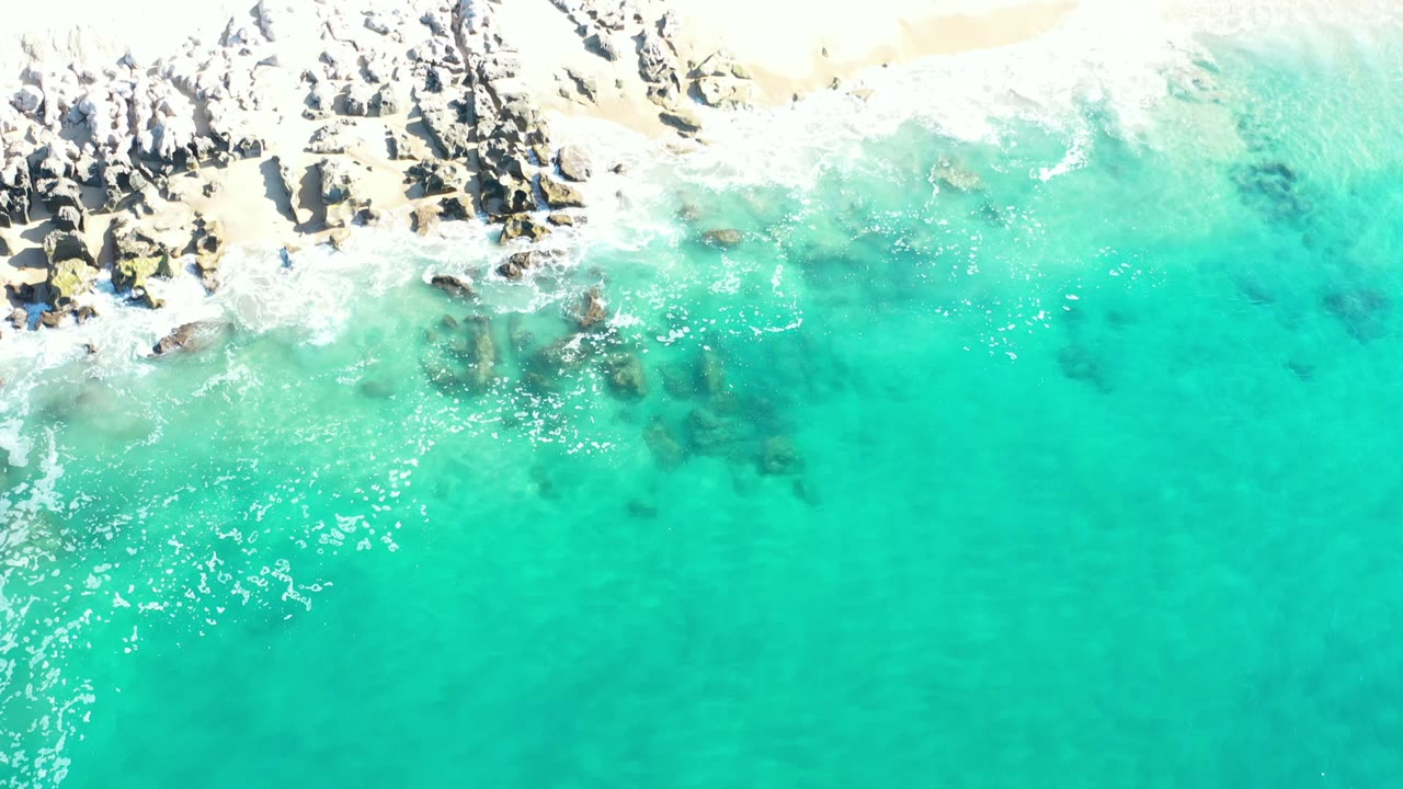 Turquoise water beside pale sand and rocky shoreline.
