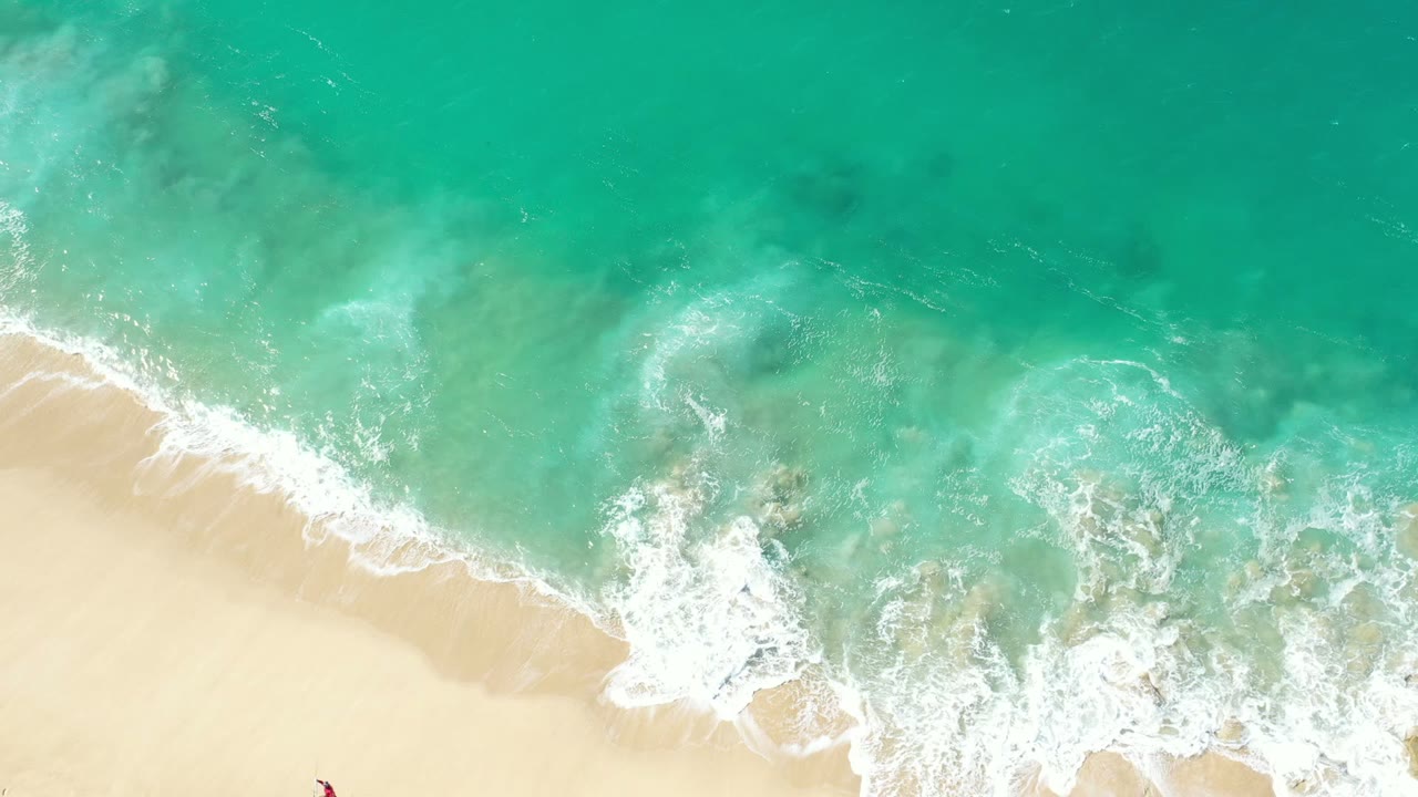 Overhead view of turquoise water and white surf meeting pale sand in Los Cabos, Mexico, with no visible people.