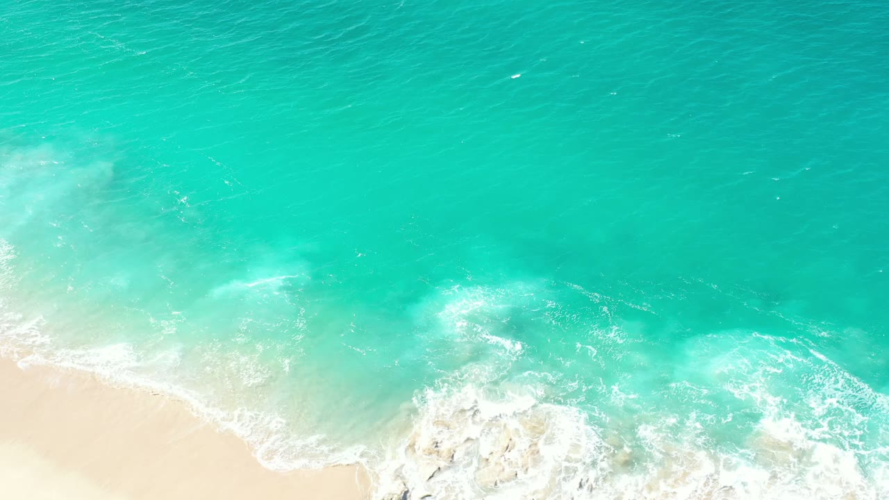Turquoise ocean surf reaching pale sand from above.
