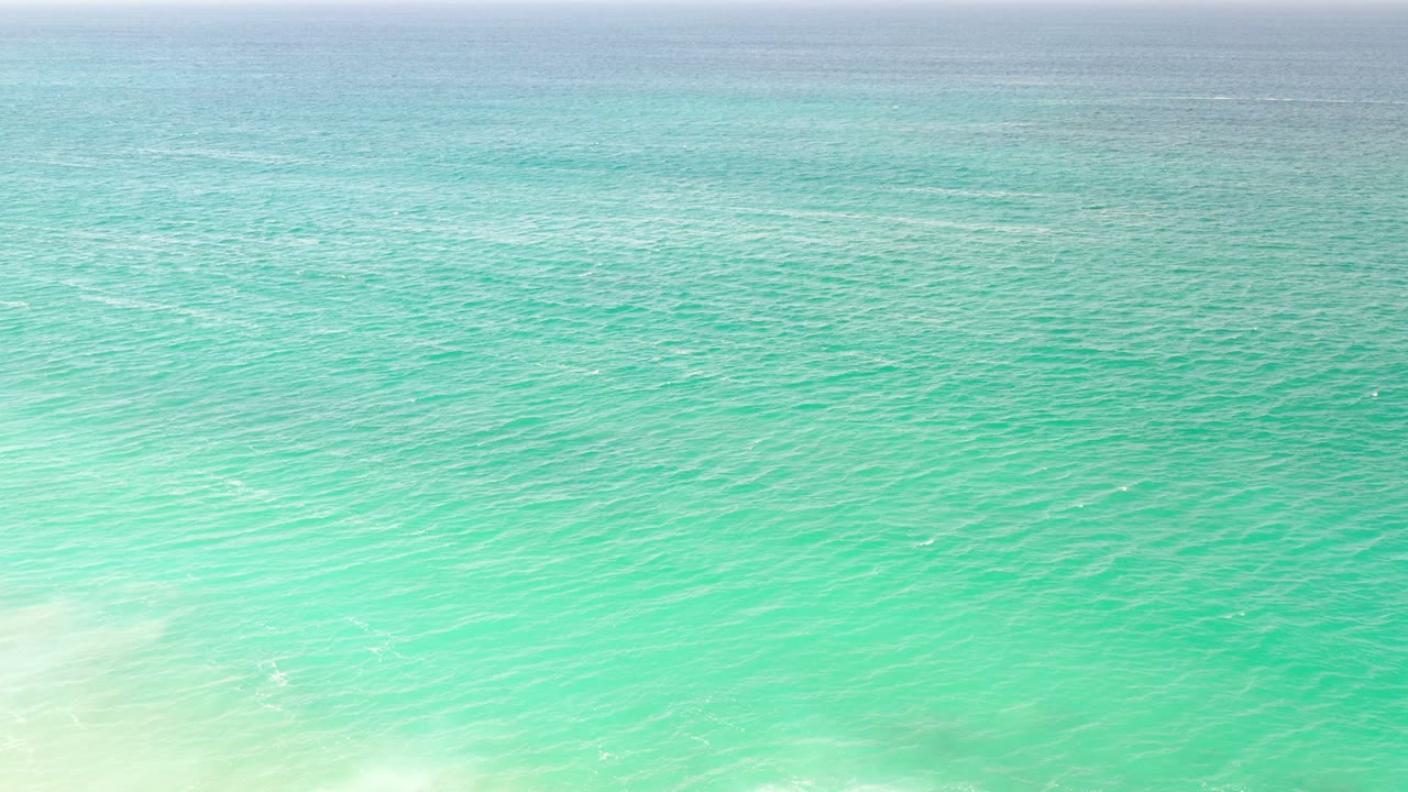 Second frame over the Los Cabos sea, showing blue-green water, faint white surf near the bottom edge, a level horizon, and no visible people.