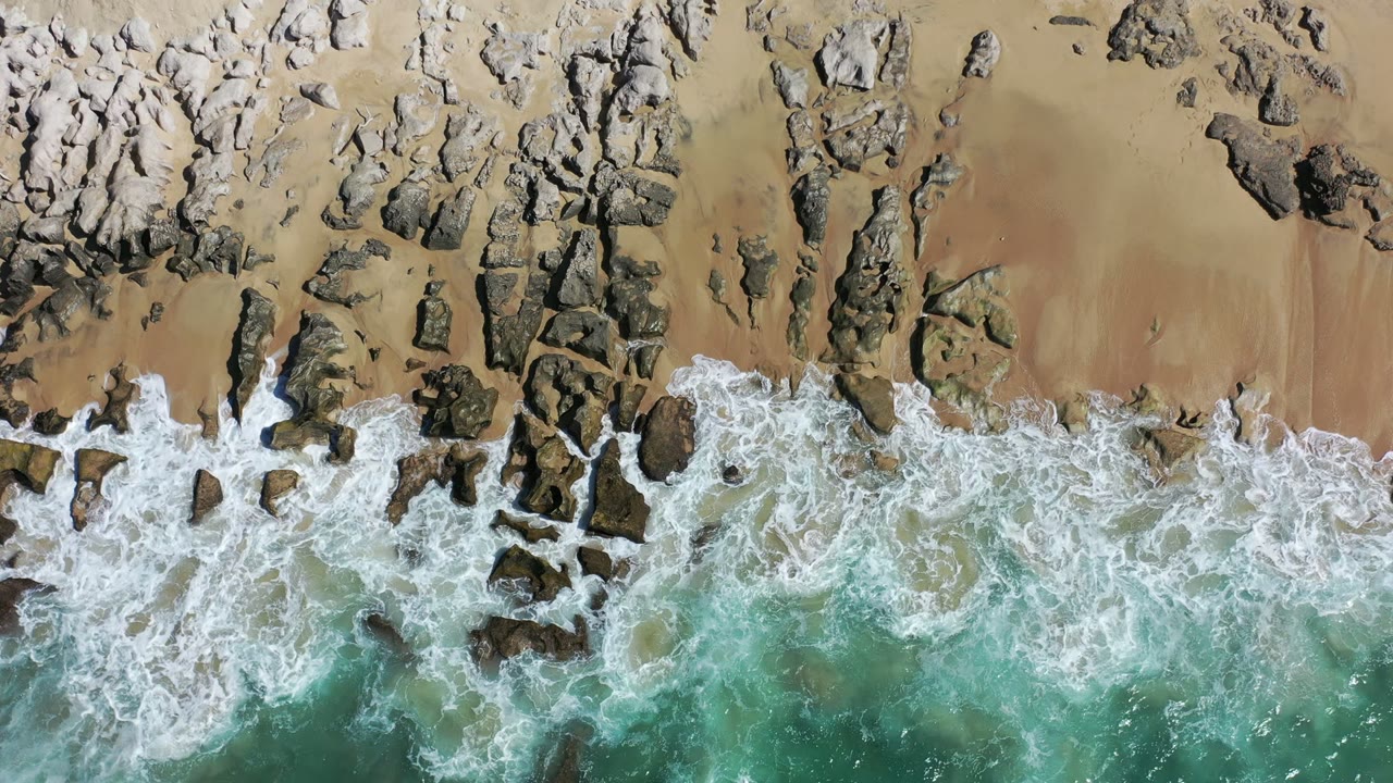 Overhead surf washing over rocks and tan beach sand.