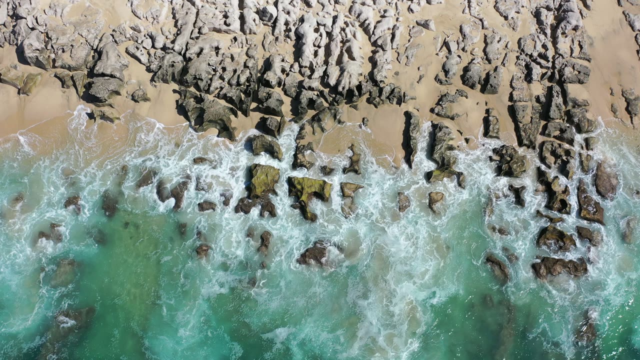 Overhead surf washing over rocks and sand.