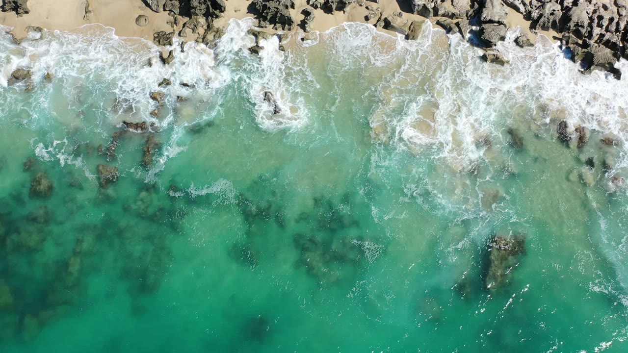 Overhead turquoise surf washing over rocks and sand.