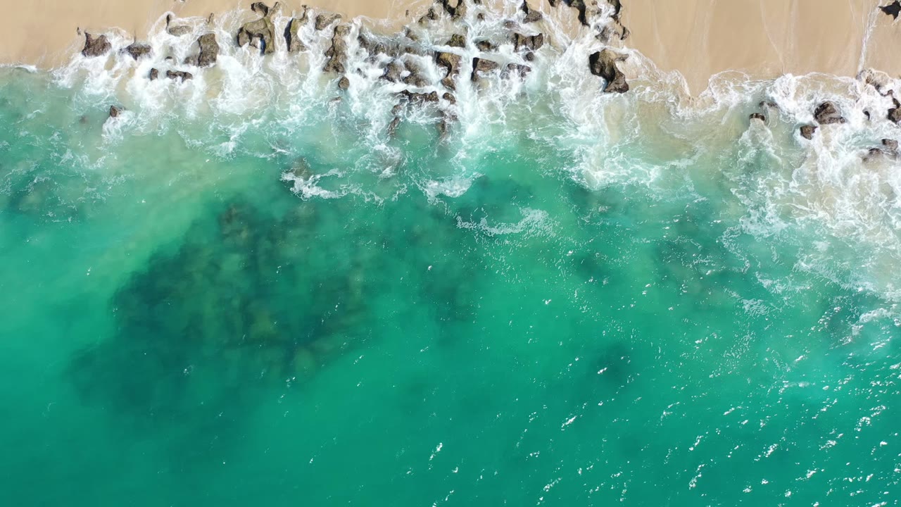 Overhead turquoise surf breaking against rocks and sand