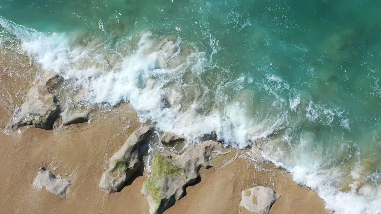 Overhead surf breaking over rocks at a sandy beach