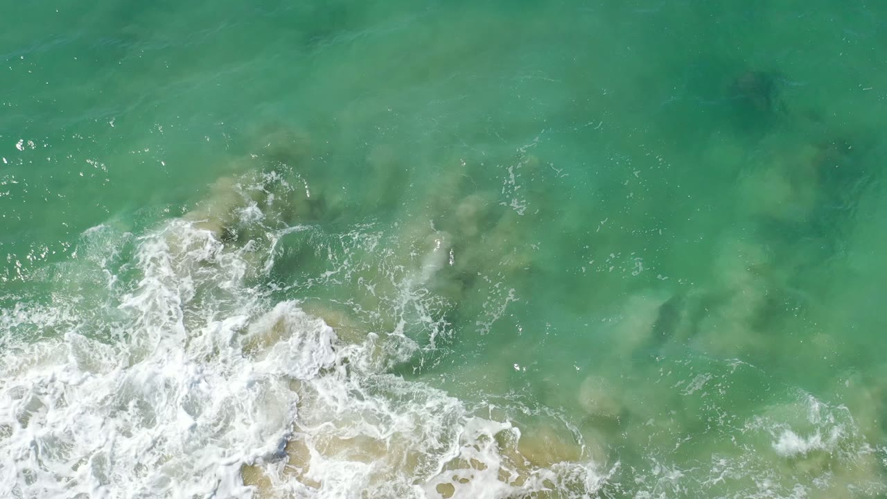 Overhead green ocean water with white surf foam near the lower edge.