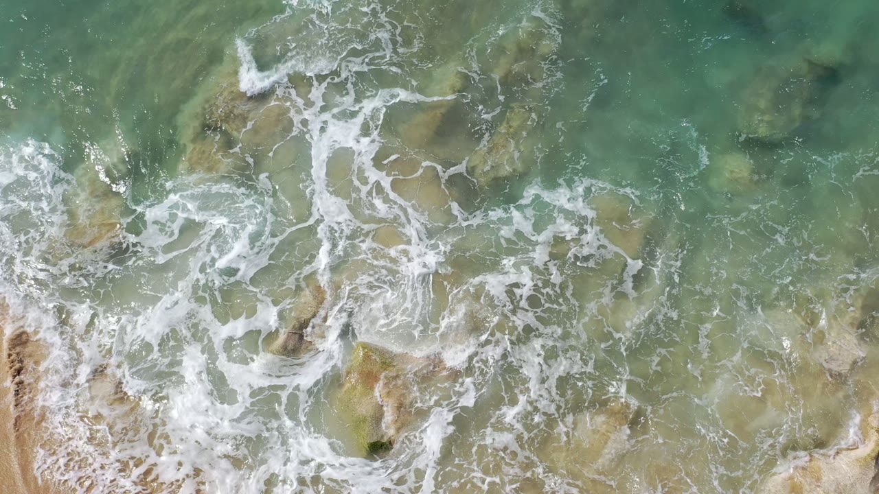 Overhead surf washing around rocks on sandy beach