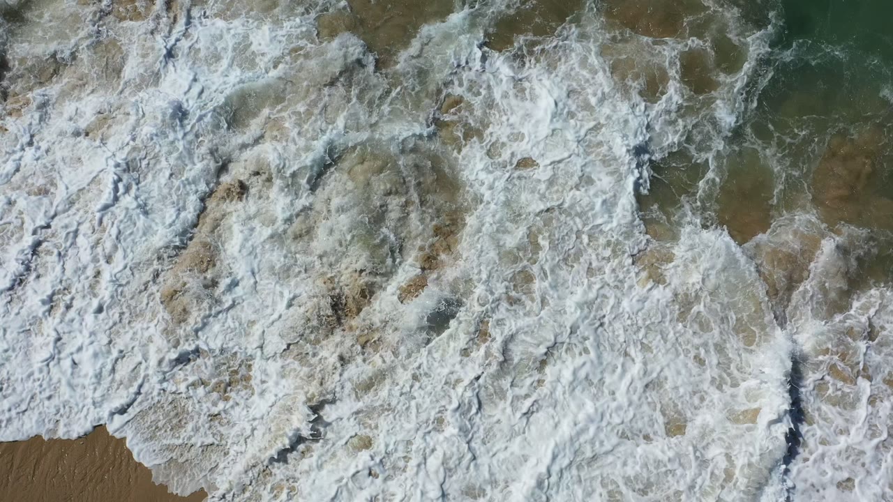 Overhead surf foam covering shallow water and wet sand.