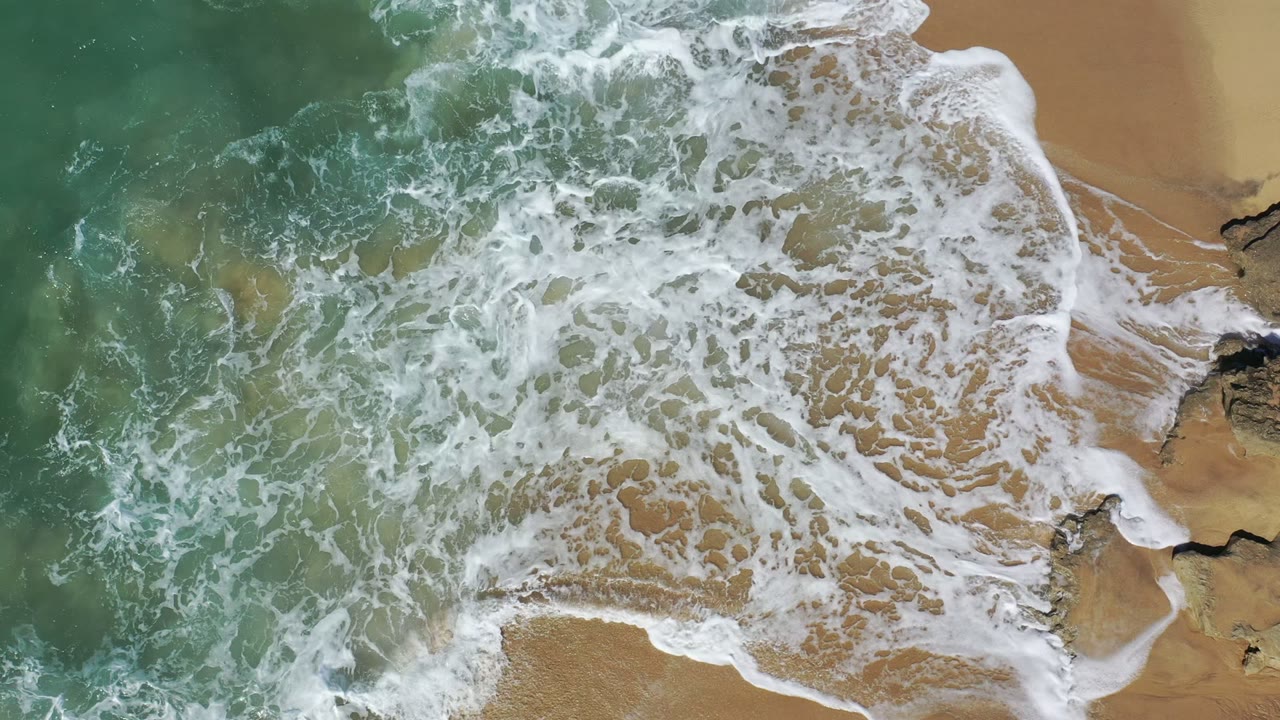 Overhead surf foam washing across tan beach sand and rocks.