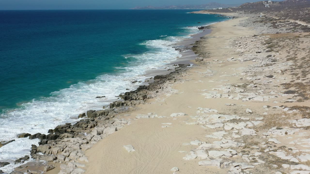 Aerial view of teal ocean, surf, rocks, and sandy beach.