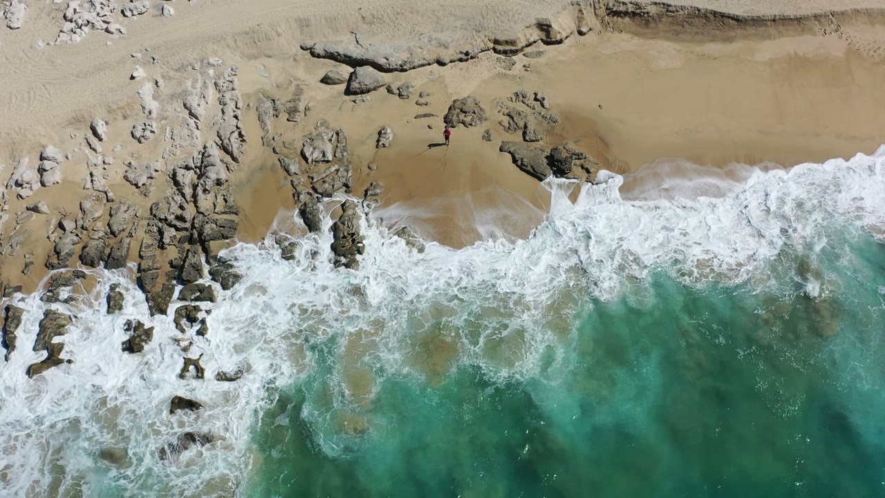 Overhead surf washing across rocks and tan beach
