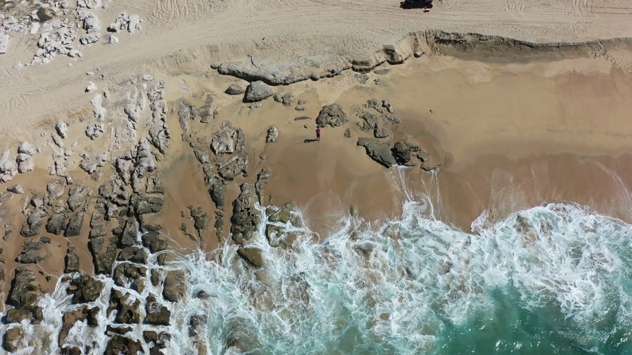 Overhead surf washing onto rocks and tan sand.