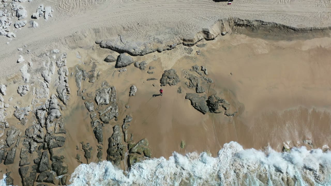 Overhead view of waves reaching a rocky sandy beach.