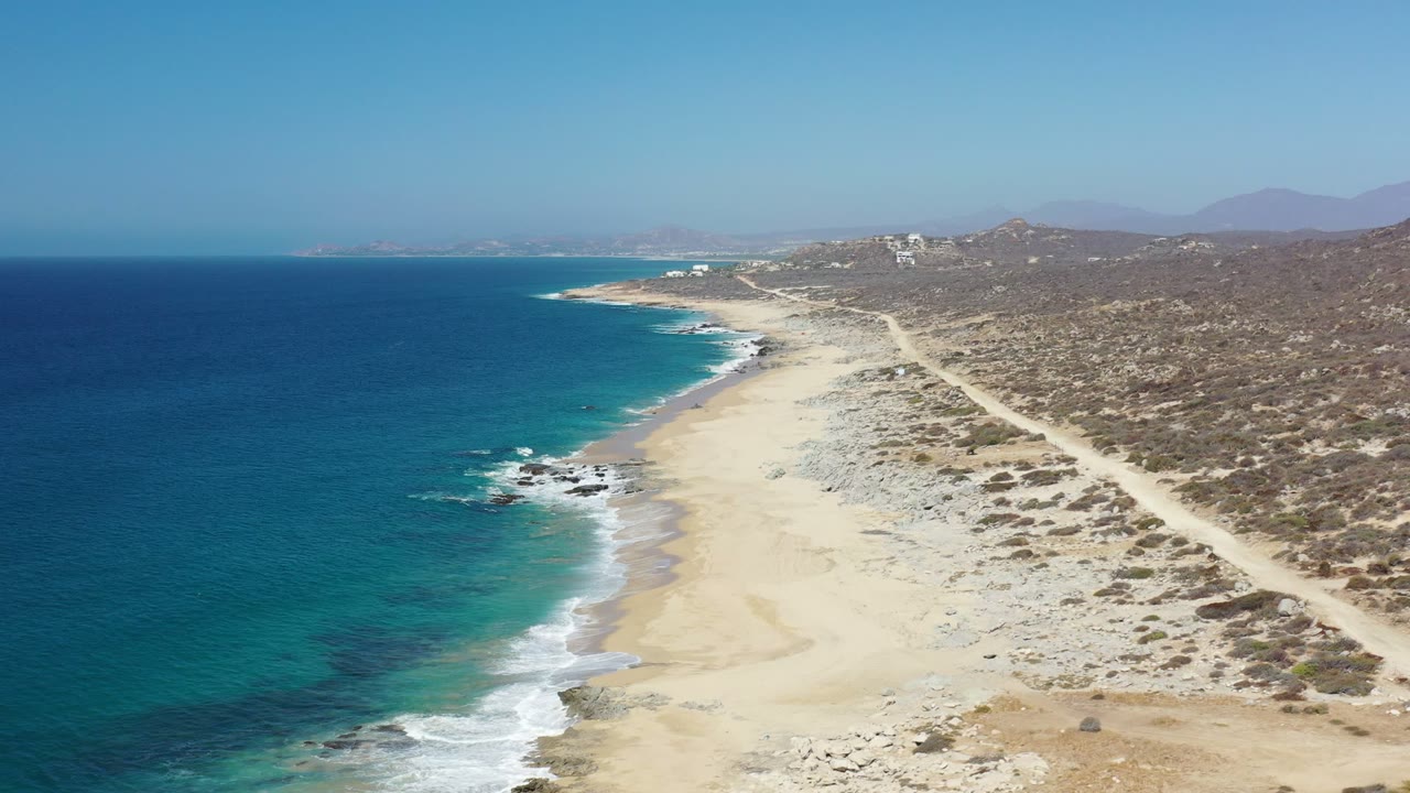 Aerial view of blue ocean beside a sandy beach and scrub-covered coast.