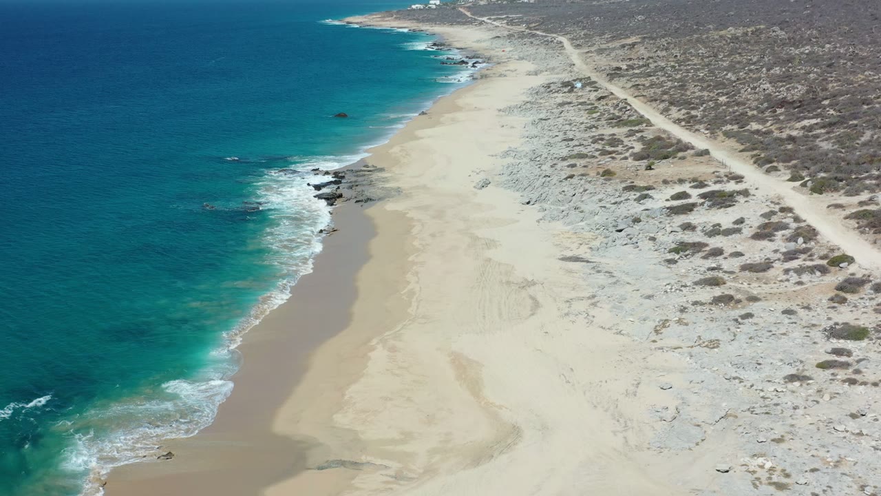 Drone angle over small waves breaking beside a wide sandy beach.