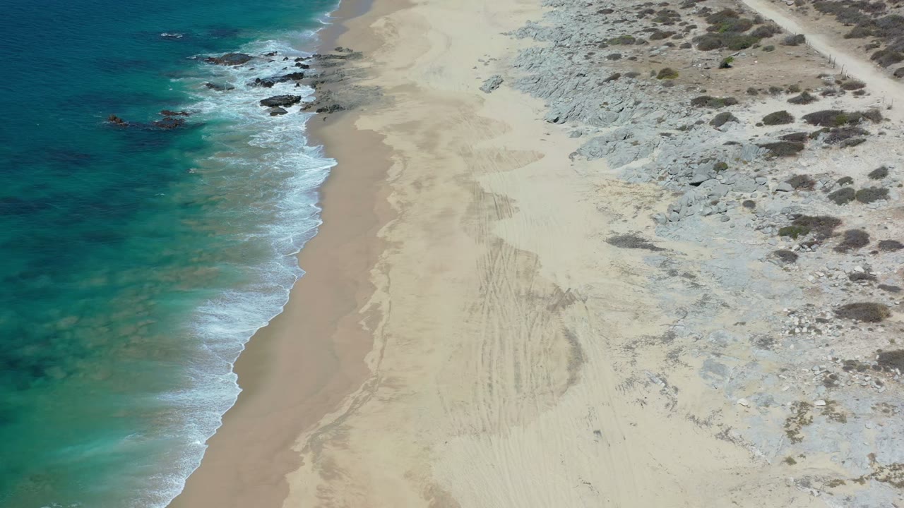 Overhead shoreline with turquoise water, wet sand, rocks, and scrub.