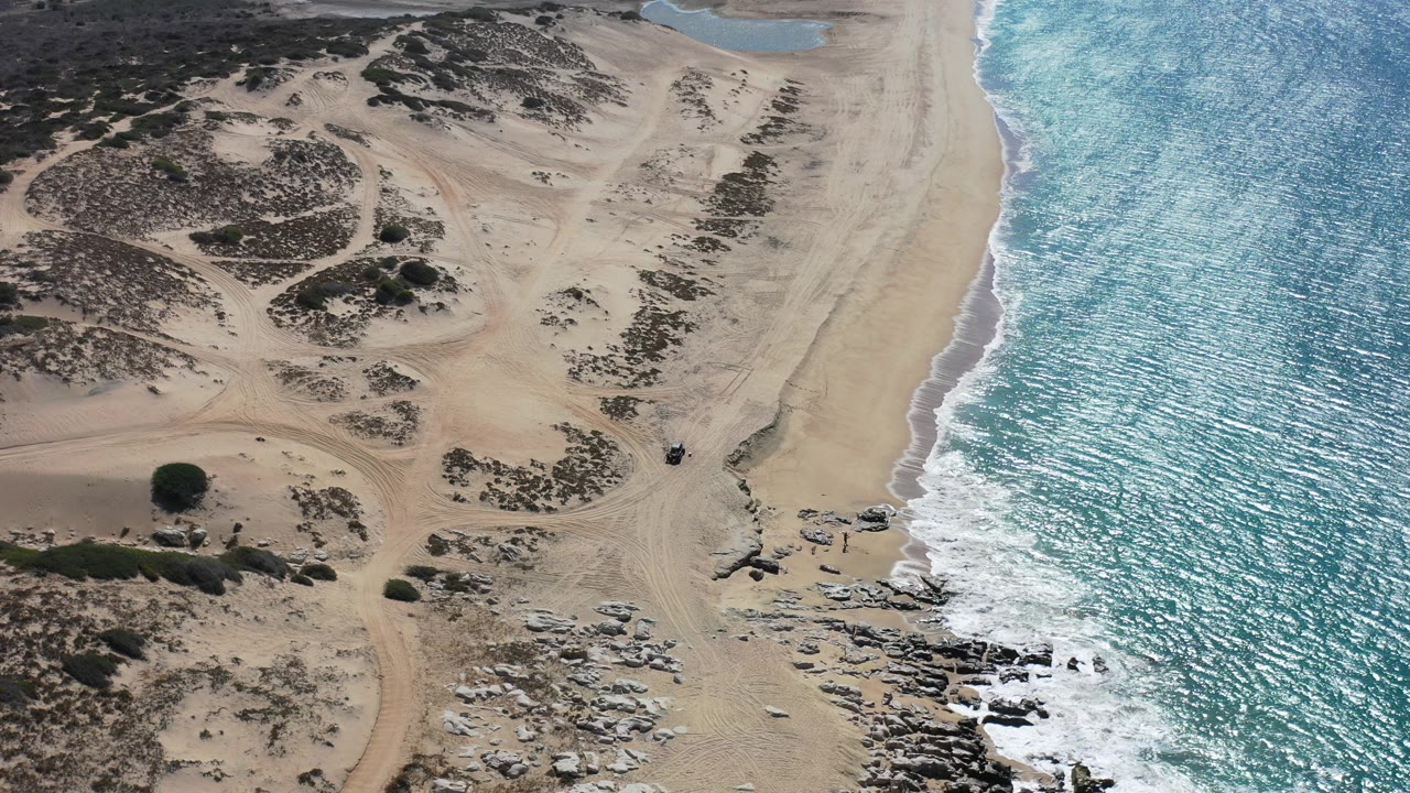Aerial view of sandy beach, dunes, rocks, and blue surf