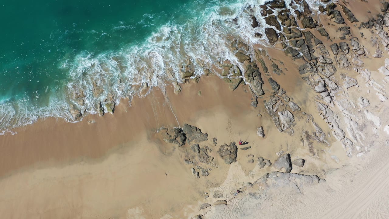 Overhead surf meeting a sandy rocky beach.