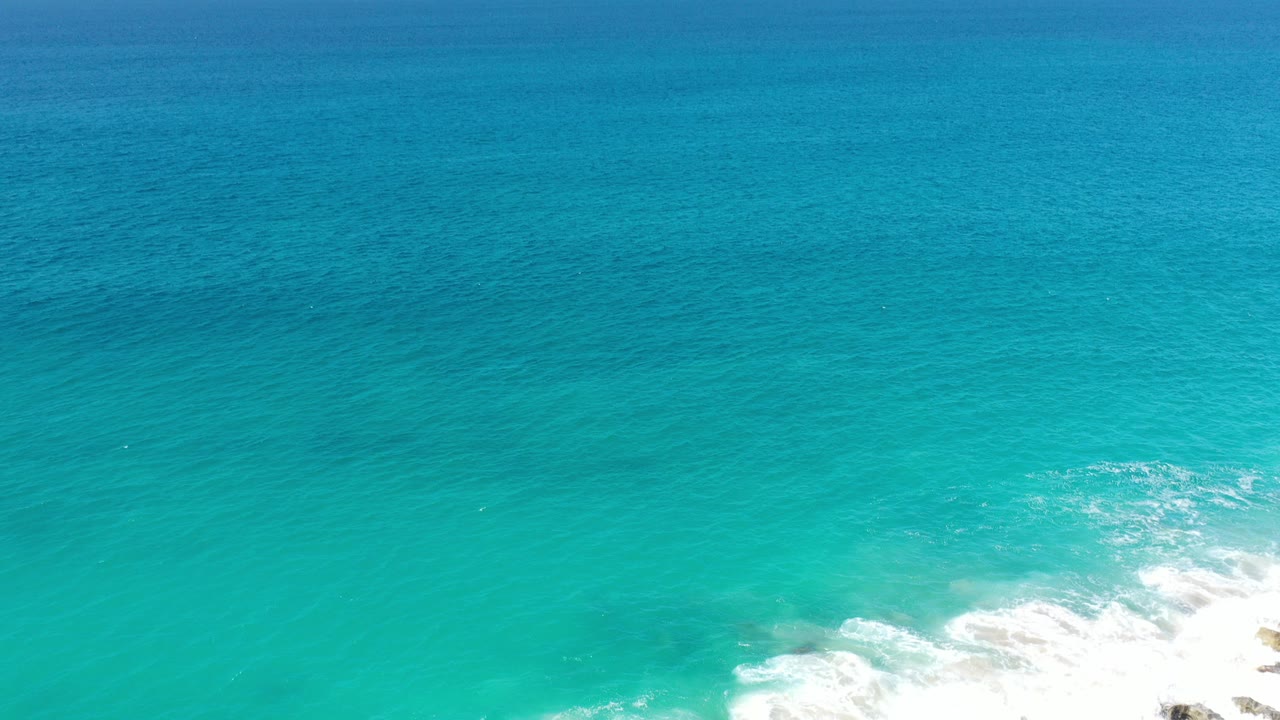 Opening frame of turquoise ocean off Los Cabos, Mexico, with white surf touching the lower edge, a level distant horizon, and no visible people.