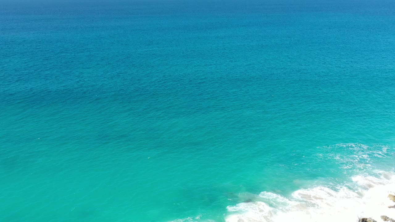 Turquoise coastal water in Los Cabos, Mexico, with a bright white surf patch near the lower right and no visible people or boats.