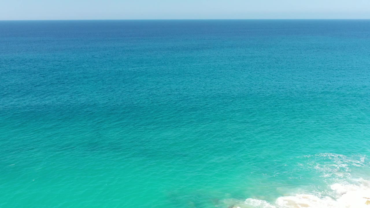 Blue-green ocean surface with white breaking water along the lower right edge.