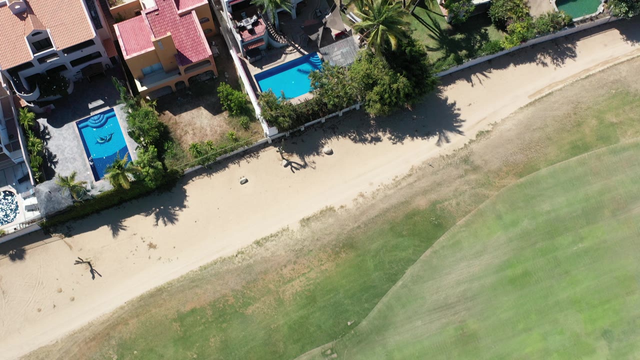Overhead view of beach houses, pools, sand, and green water.