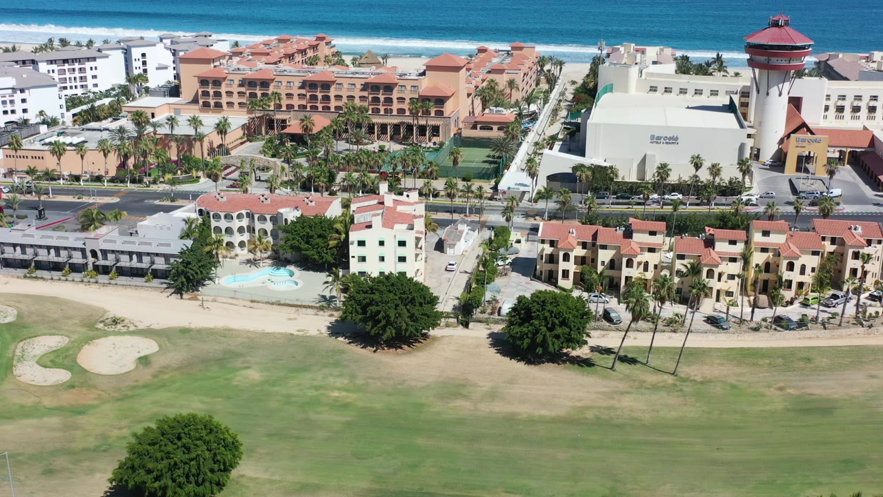 Aerial view of golf course villas, resort buildings, and ocean surf.