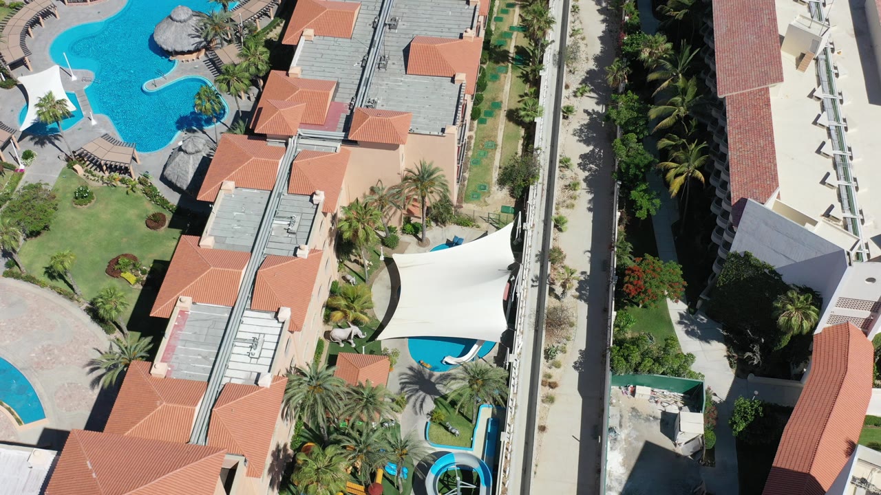Overhead resort buildings, pools, palms, and sand.
