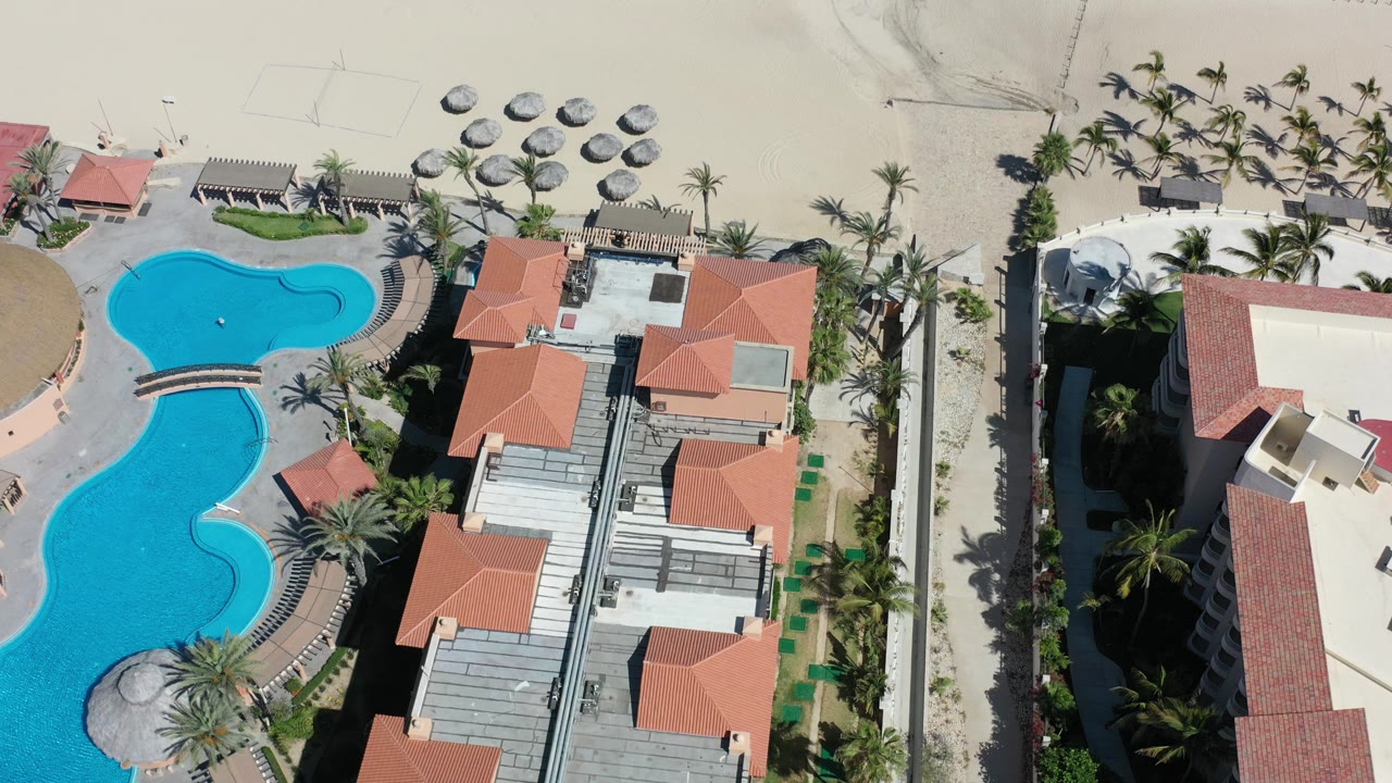 Overhead view of a beach house, blue pool, palms, and sand.