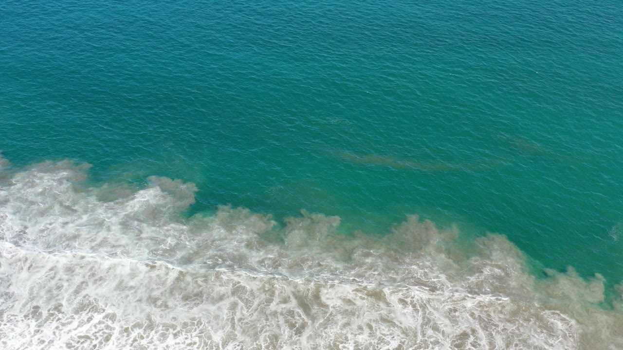 Overhead Los Cabos ocean view with turquoise water above a band of foamy white surf, no visible people.