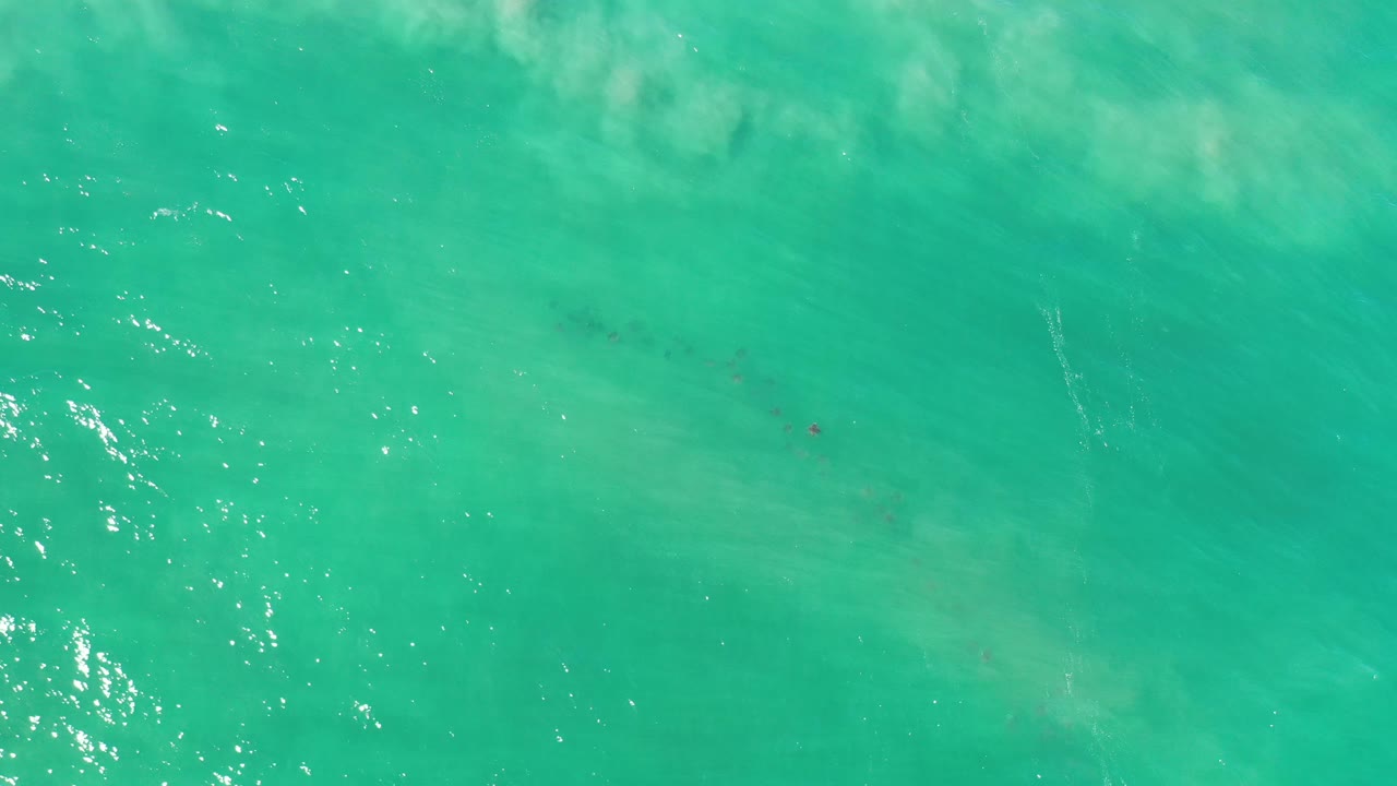 Overhead turquoise water with bright glare and faint fish below.