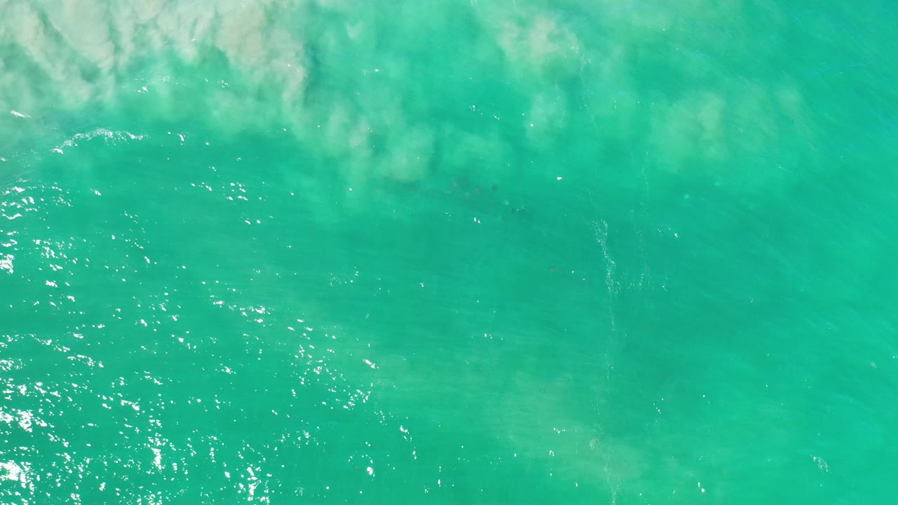 Overhead view of turquoise water in Los Cabos, Mexico with pale reflected cloud shapes near the upper left, scattered sunlight on the surface, and no visible people.