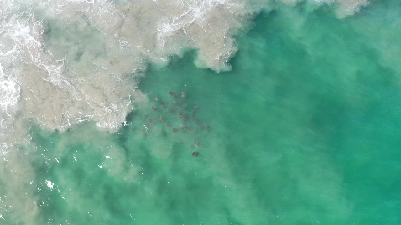 Aerial water view with white foam, turquoise shallows, and open clear sea.
