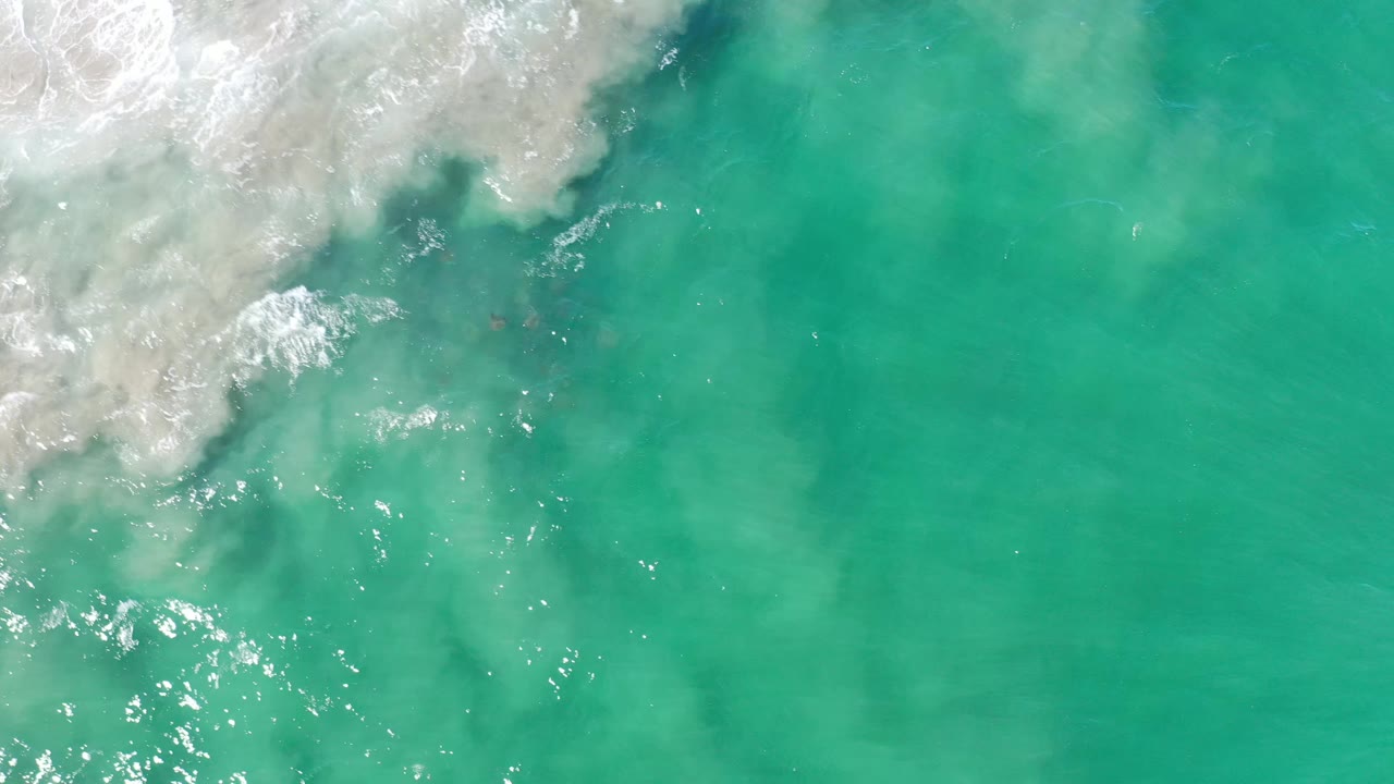 Los Cabos aerial frame with foamy white water at the upper left, clear green ocean across the frame, and no visible people.