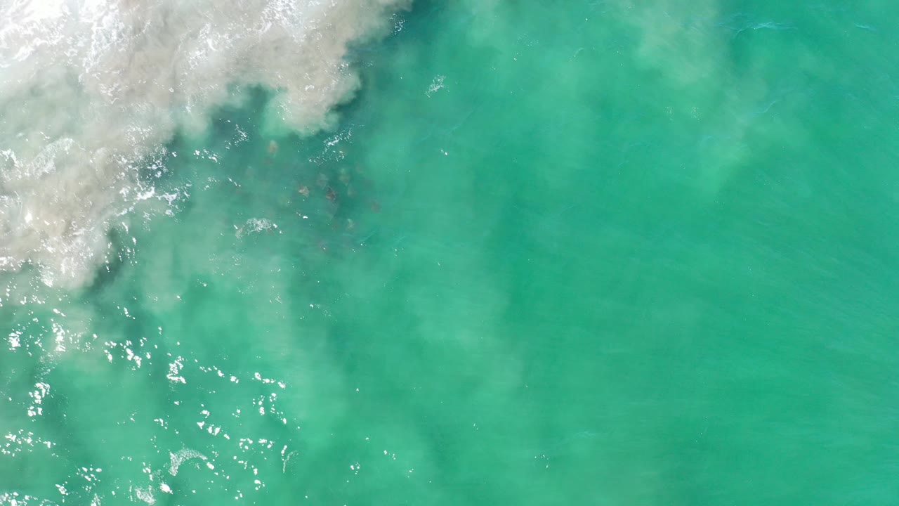 Turquoise water with surf foam along the left edge and scattered sun sparkle.