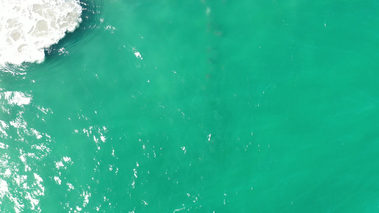 Turquoise-green ocean seen from above with white surf at the upper left.