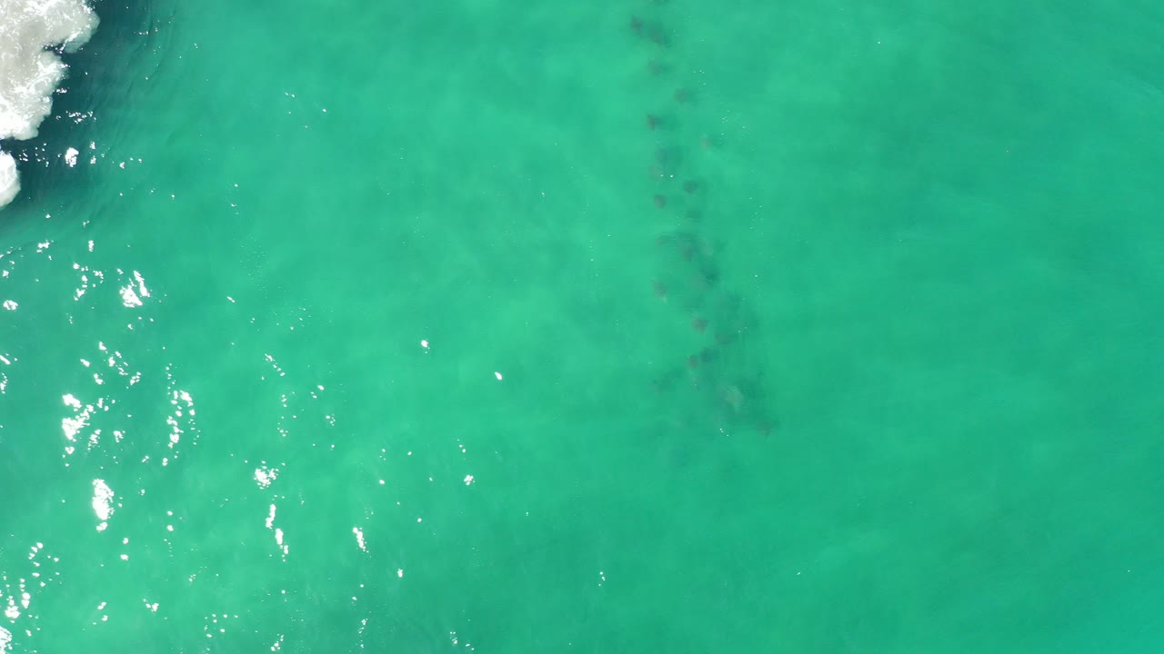 Turquoise ocean water with sun glints and white foam at upper left.