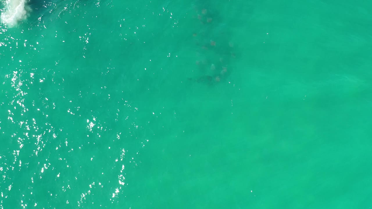 Top-down Los Cabos ocean frame with a vertical band of bright reflected sunlight over green water and no visible people.