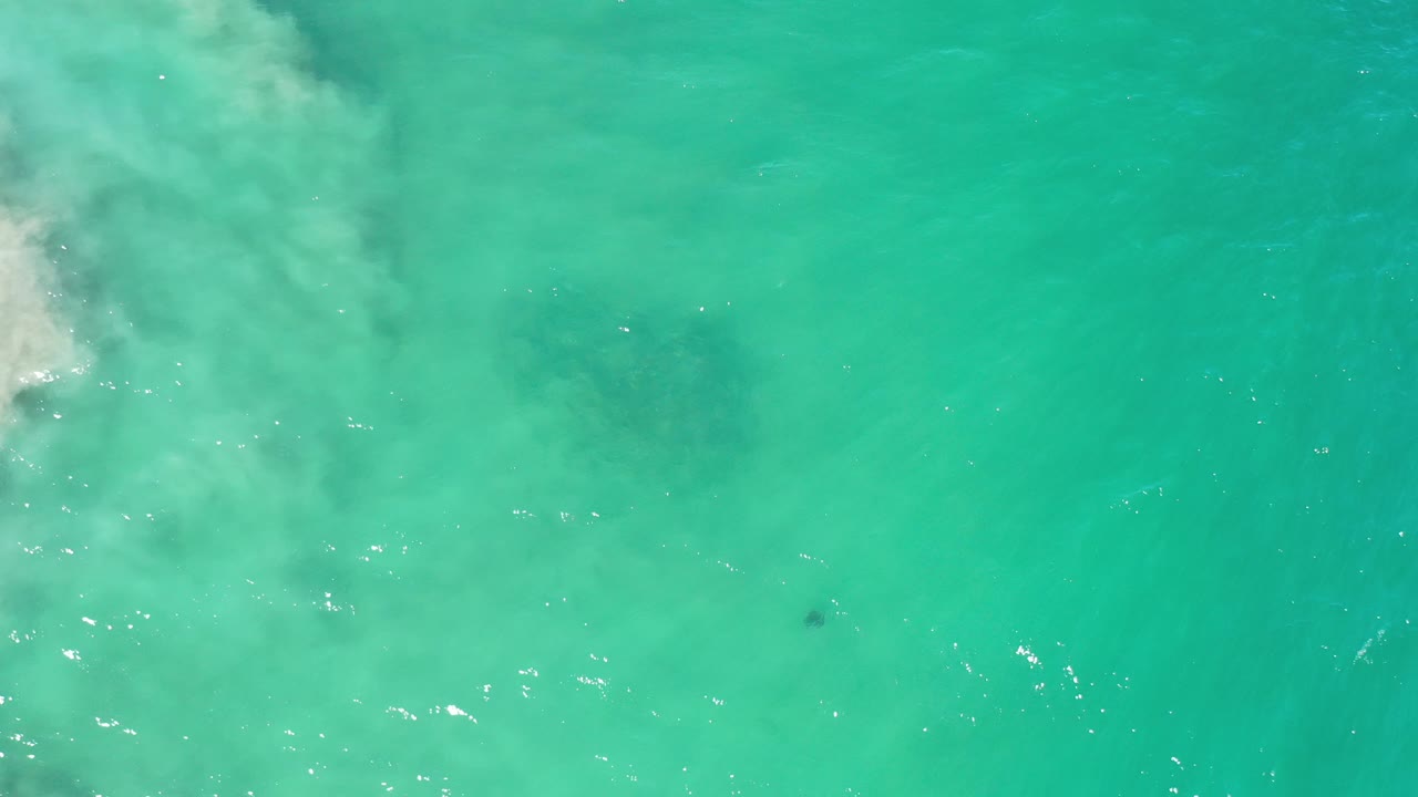 Turquoise ocean water with foam entering from the upper left.