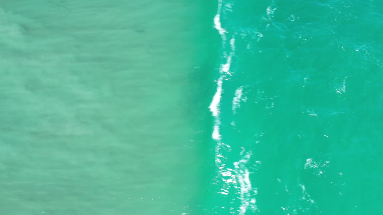 Turquoise-green water with a vertical strip of white surf foam.