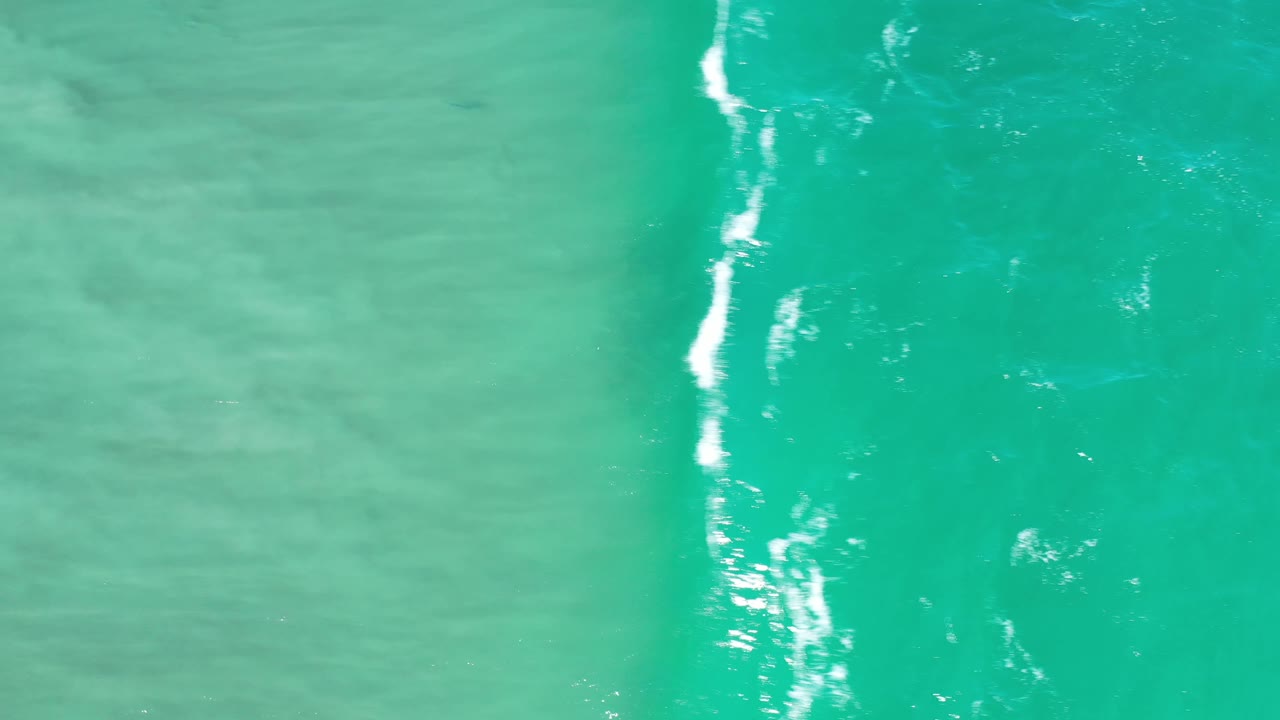 Green ocean water in Los Cabos, Mexico with broken white foam streaks running vertically through the frame and no visible people.
